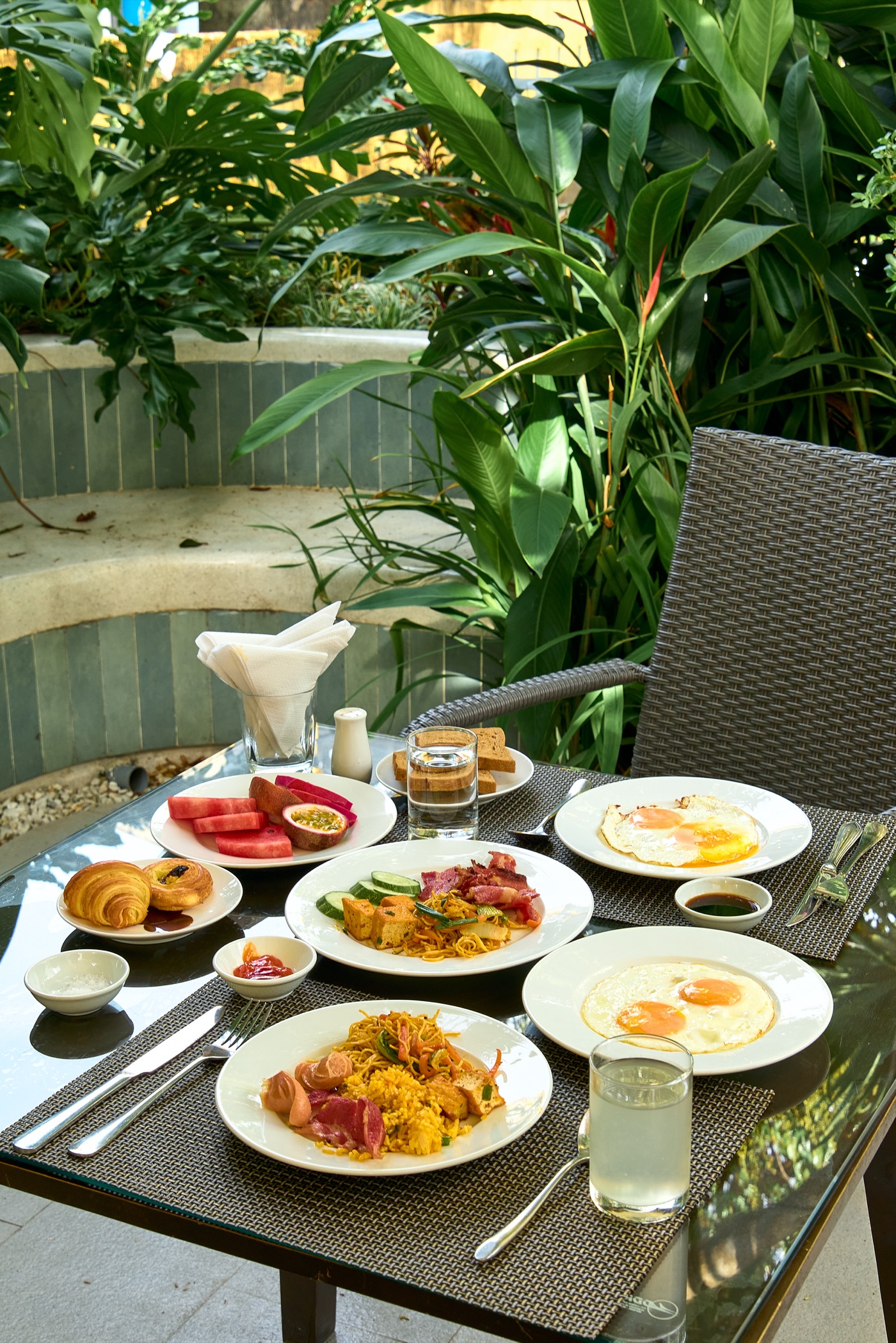 Staff in a green áo dài serving a table set for breakfast in the garden