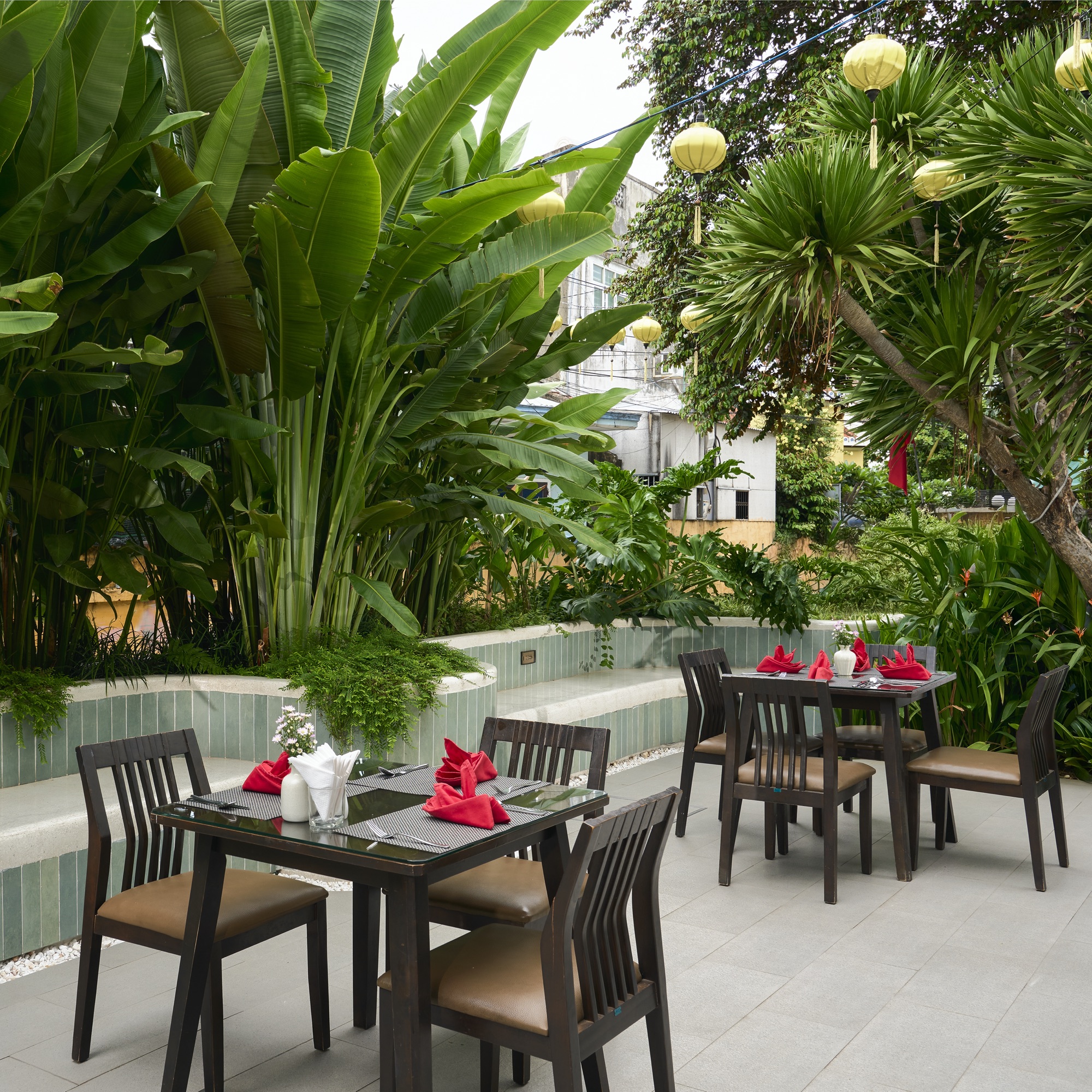 Green Restaurant tables set under hanging lanterns and banana palms