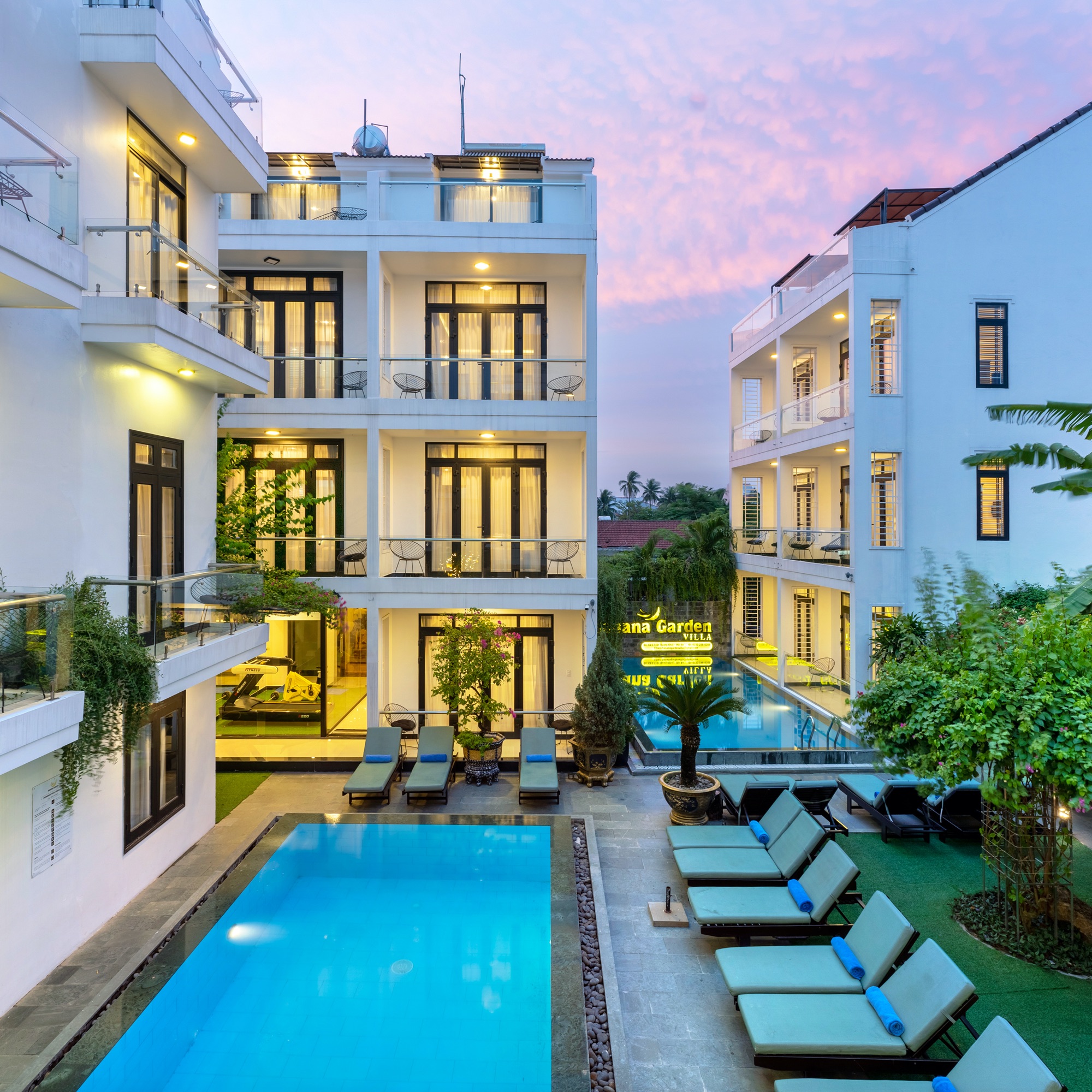 Both courtyard pools and the lit-up Banana Garden Villa sign at dusk